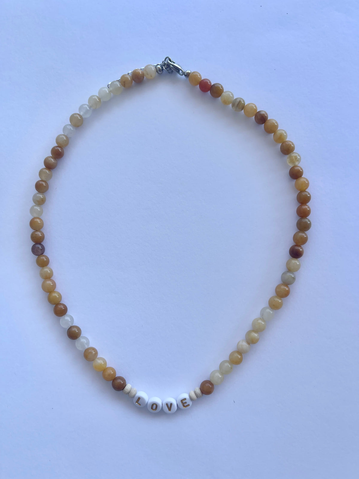 Honey jade LOVE necklace laid flat, mustard and cream beads with white letter beads
